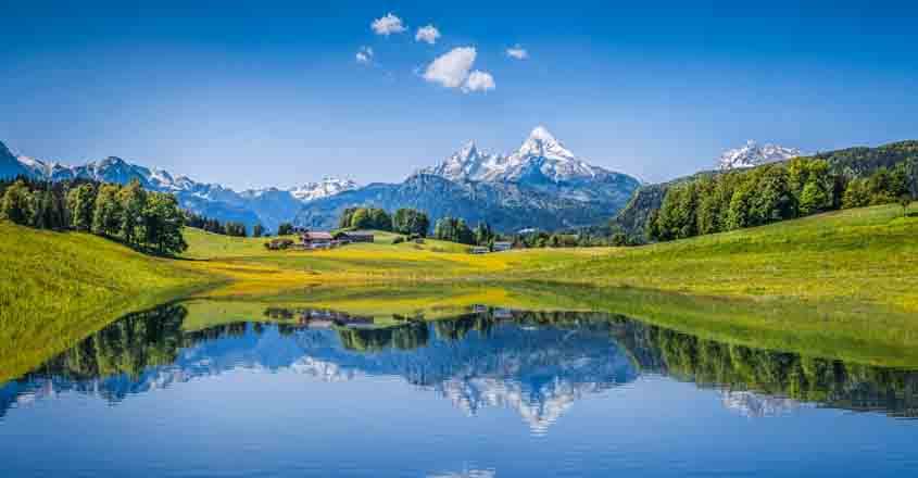 Panoramic view of idyllic summer landscape in the Alps with clear mountain lake and fresh green mountain pastures in the background